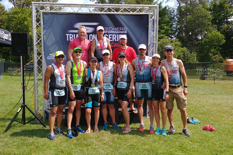 Group of DRTC members at an Ironman standing on a podium wearing their medals